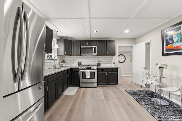 kitchen with light stone countertops, stainless steel appliances, tasteful backsplash, a sink, and light wood-type flooring