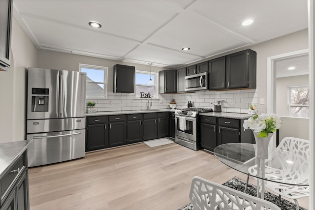 kitchen with light wood-style flooring, a sink, tasteful backsplash, and appliances with stainless steel finishes