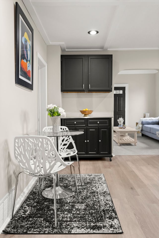 kitchen featuring open floor plan, light countertops, arched walkways, light wood-style flooring, and dark cabinets