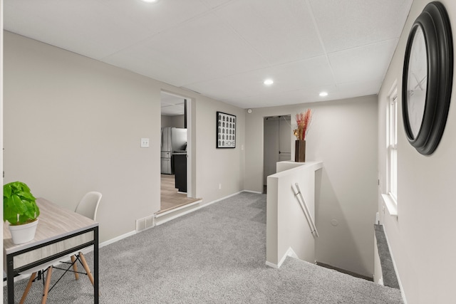 corridor with baseboards, visible vents, an upstairs landing, and carpet floors