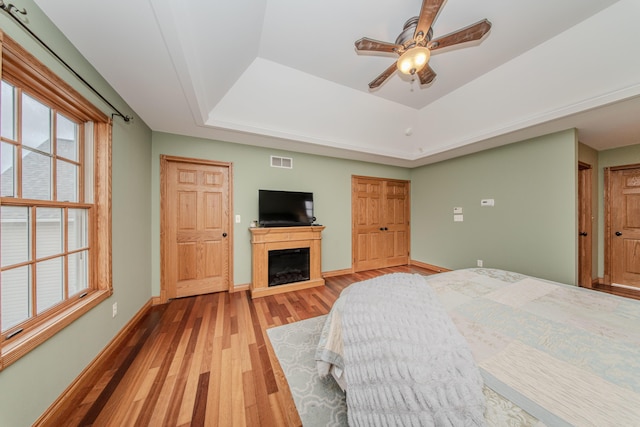 5050 Pleasant Lake Rd, Ann Arbor, MI 48103 - bedroom featuring a tray ceiling, wood finished floors, a fireplace, and a ceiling fan