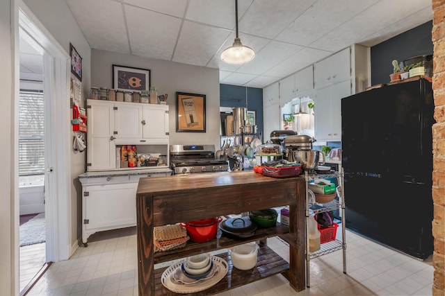 kitchen featuring stainless steel stove, white cabinetry, a drop ceiling, and decorative light fixtures