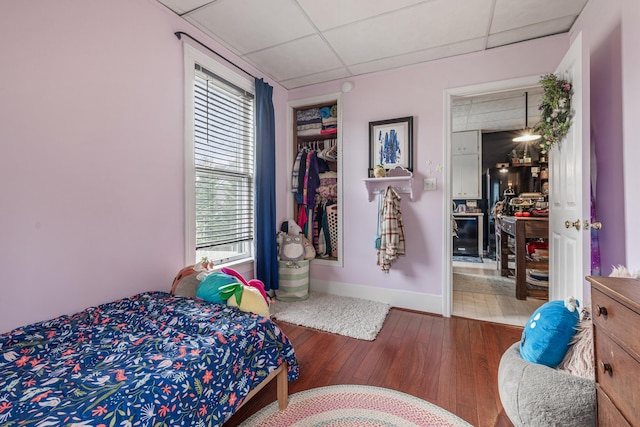 bedroom featuring baseboards, wood finished floors, and a paneled ceiling