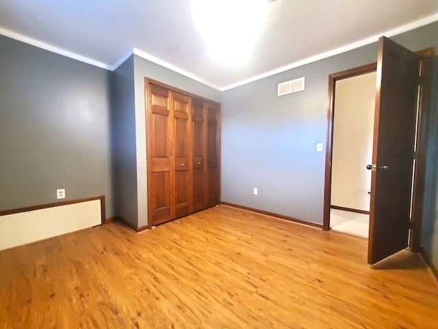 unfurnished bedroom featuring a closet, visible vents, light wood finished floors, baseboards, and ornamental molding