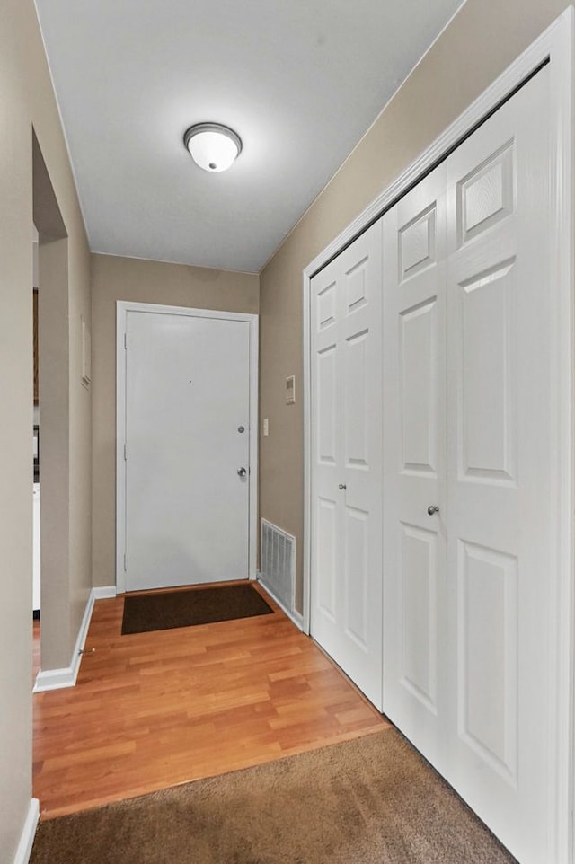 doorway with baseboards, carpet flooring, visible vents, and wood finished floors