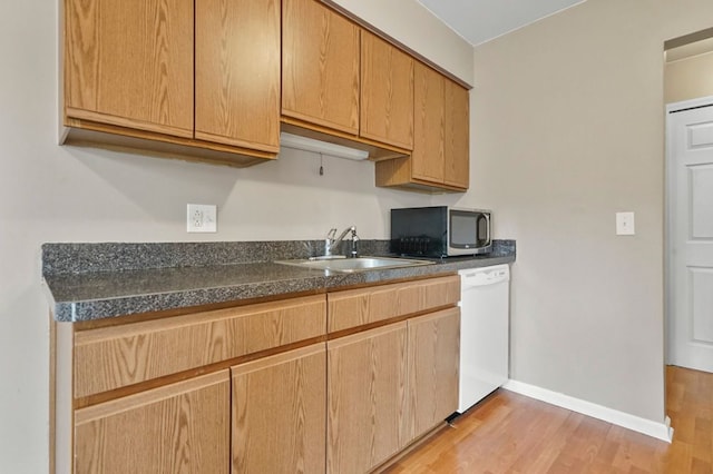 kitchen with a sink, white dishwasher, light wood-style flooring, baseboards, and dark countertops