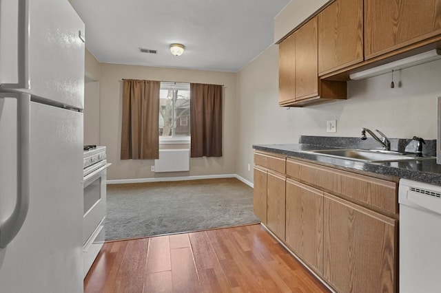 kitchen featuring visible vents, light wood-style flooring, white appliances, dark countertops, and a sink