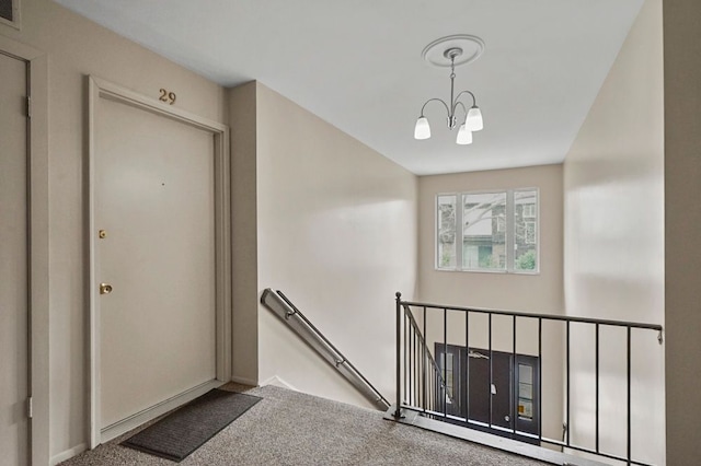 hallway featuring a notable chandelier, an upstairs landing, and carpet flooring