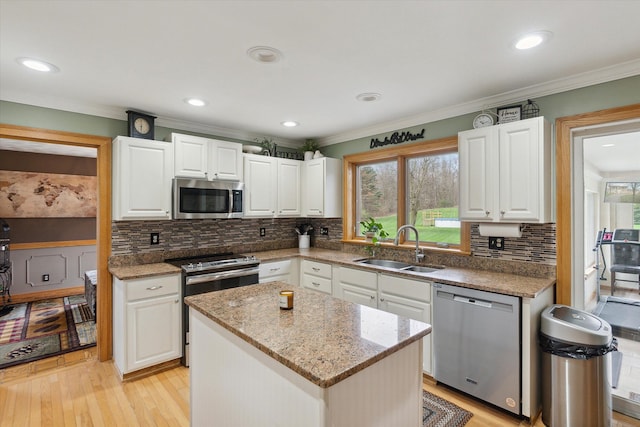 kitchen featuring appliances with stainless steel finishes, light wood finished floors, a sink, and white cabinets