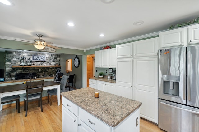 kitchen with stainless steel refrigerator with ice dispenser, ceiling fan, crown molding, light wood-style flooring, and light stone counters