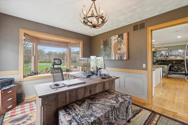 office with an inviting chandelier, wainscoting, light wood-type flooring, and visible vents