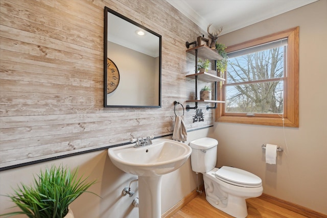 half bathroom featuring baseboards, ornamental molding, toilet, a sink, and wood finished floors