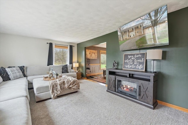 living room with a glass covered fireplace, carpet flooring, and baseboards