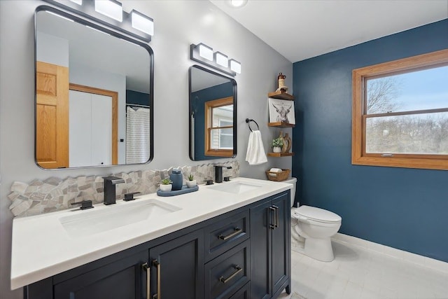 bathroom featuring toilet, double vanity, a sink, and baseboards