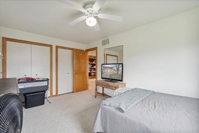 carpeted bedroom with visible vents, multiple closets, and a ceiling fan