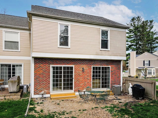 rear view of house with central AC, brick siding, and fence