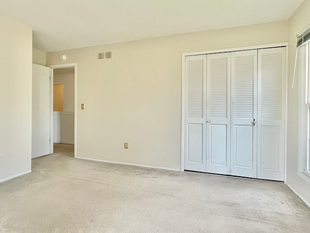 unfurnished bedroom featuring baseboards, visible vents, a closet, and light colored carpet