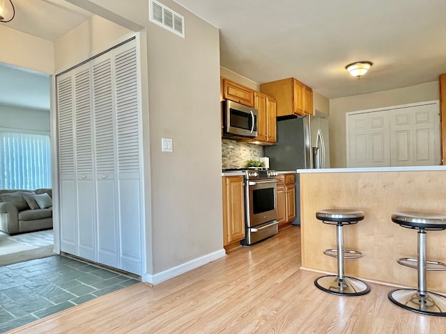 kitchen featuring appliances with stainless steel finishes, visible vents, light wood finished floors, and backsplash