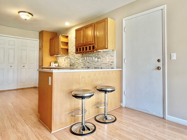 kitchen featuring a peninsula, light wood-style flooring, decorative backsplash, and light countertops
