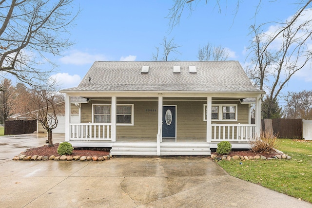 bungalow-style house featuring roof with shingles, a porch, driveway, and fence