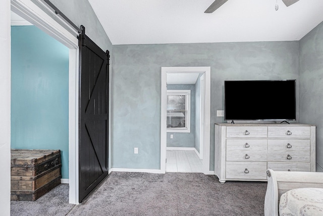unfurnished bedroom featuring baseboards, carpet floors, ensuite bath, a barn door, and a ceiling fan