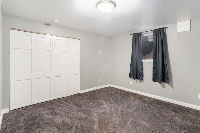 unfurnished bedroom featuring baseboards, a closet, and dark colored carpet
