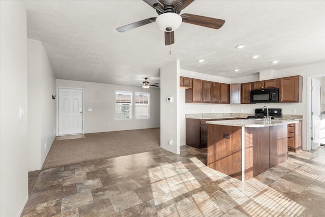 kitchen with an island with sink, light countertops, black microwave, stove, and ceiling fan