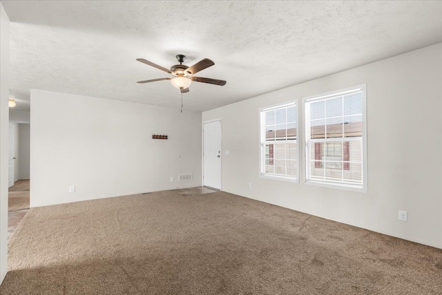 interior space with a textured ceiling, visible vents, a ceiling fan, and light colored carpet