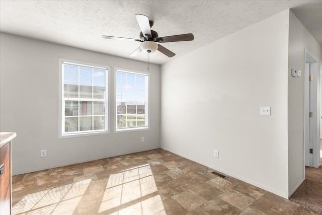 empty room with a textured ceiling, visible vents, stone finish floor, and a ceiling fan
