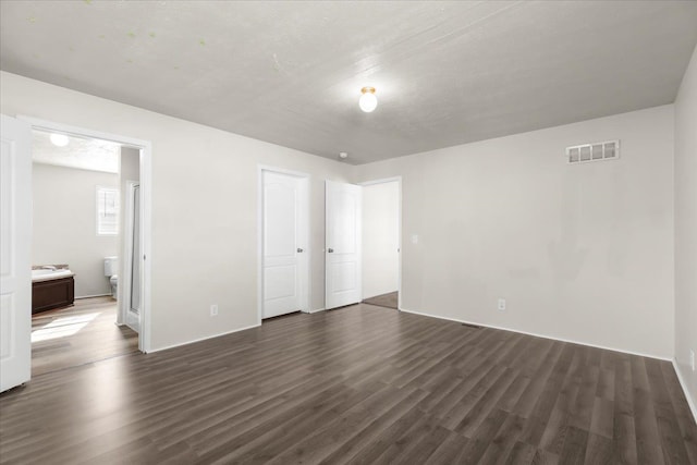 unfurnished bedroom with connected bathroom, visible vents, and dark wood-type flooring
