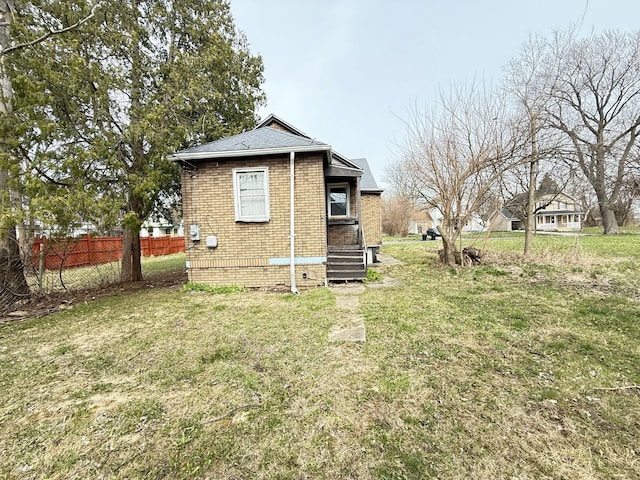 view of side of home with a yard, fence, brick siding, and roof with shingles