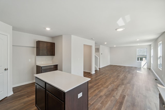 kitchen featuring a kitchen island, dark wood finished floors, dark brown cabinets, light countertops, and baseboards