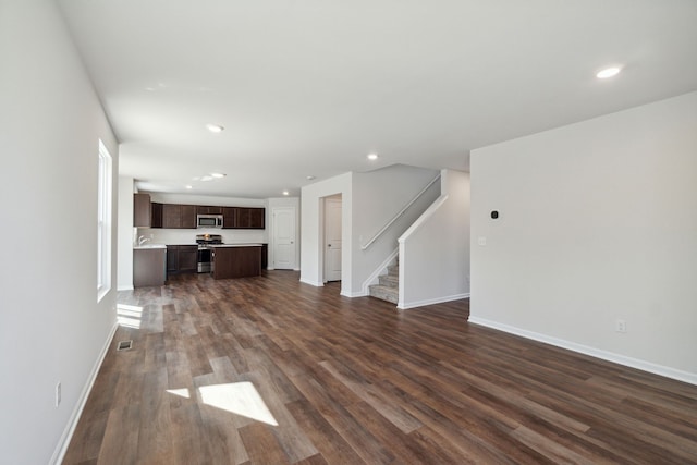 unfurnished living room with stairs, recessed lighting, baseboards, and dark wood-type flooring