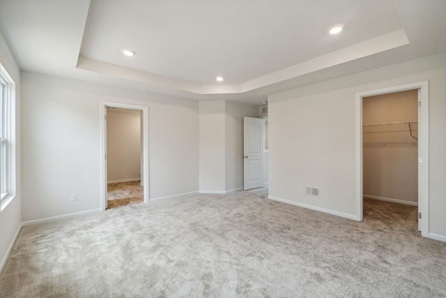 unfurnished bedroom featuring a raised ceiling, visible vents, carpet, and a spacious closet