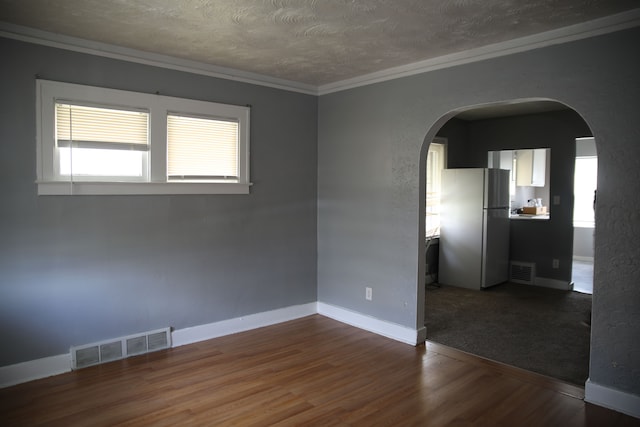 unfurnished room featuring arched walkways, visible vents, crown molding, and wood finished floors