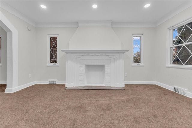 unfurnished living room featuring carpet floors, a fireplace, visible vents, and ornamental molding