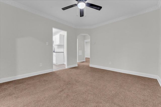 spare room with light colored carpet, ornamental molding, baseboards, arched walkways, and a ceiling fan
