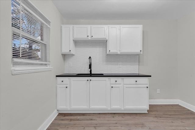 kitchen with white cabinetry, a sink, dark countertops, and light wood finished floors