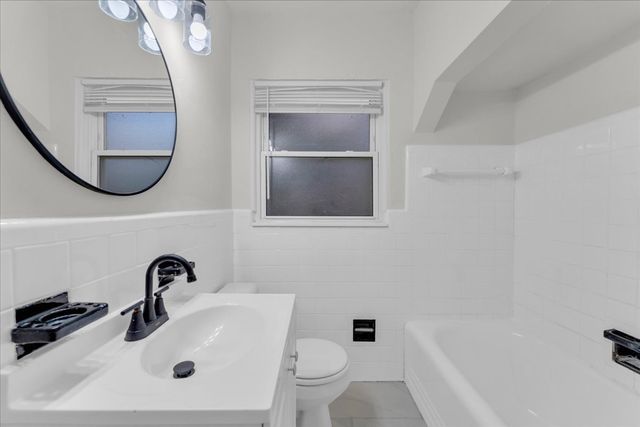 full bathroom with toilet, vanity, washtub / shower combination, wainscoting, and tile walls