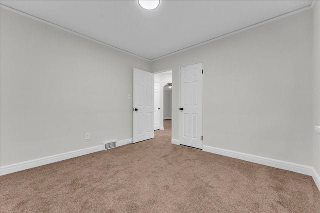carpeted empty room featuring baseboards, ornamental molding, and visible vents