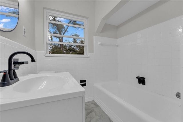full bathroom featuring shower / bathing tub combination, vanity, tile walls, marble finish floor, and wainscoting
