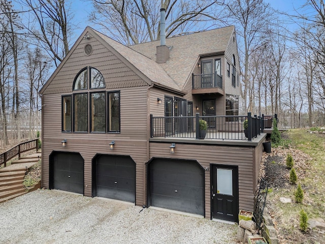 view of front facade with an attached garage, a shingled roof, gravel driveway, and a balcony