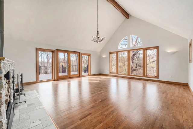 unfurnished living room with a notable chandelier, light wood-type flooring, a fireplace, beam ceiling, and high vaulted ceiling