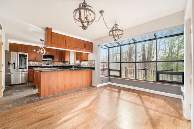 kitchen with a notable chandelier, backsplash, dark countertops, brown cabinets, and appliances with stainless steel finishes