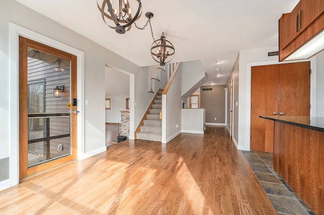 foyer entrance with stairway, baseboards, an inviting chandelier, and wood finished floors