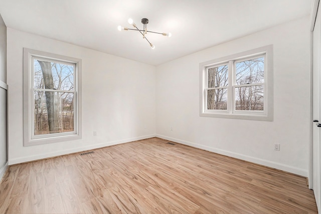 unfurnished room with a chandelier, a wealth of natural light, light wood-type flooring, and baseboards