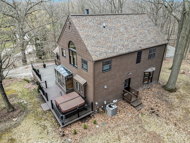 back of house featuring central air condition unit, a jacuzzi, a wooden deck, and roof with shingles