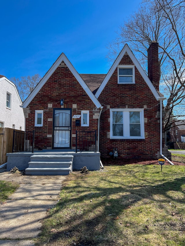 tudor home with a front yard, fence, brick siding, and a chimney