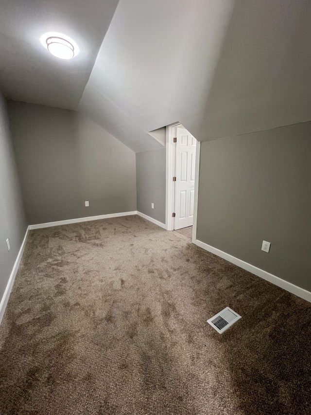additional living space with carpet flooring, baseboards, vaulted ceiling, and visible vents