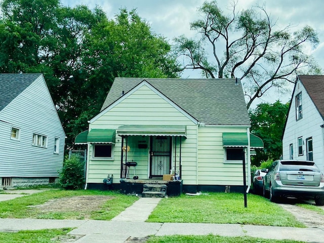 bungalow-style home with a front lawn and roof with shingles